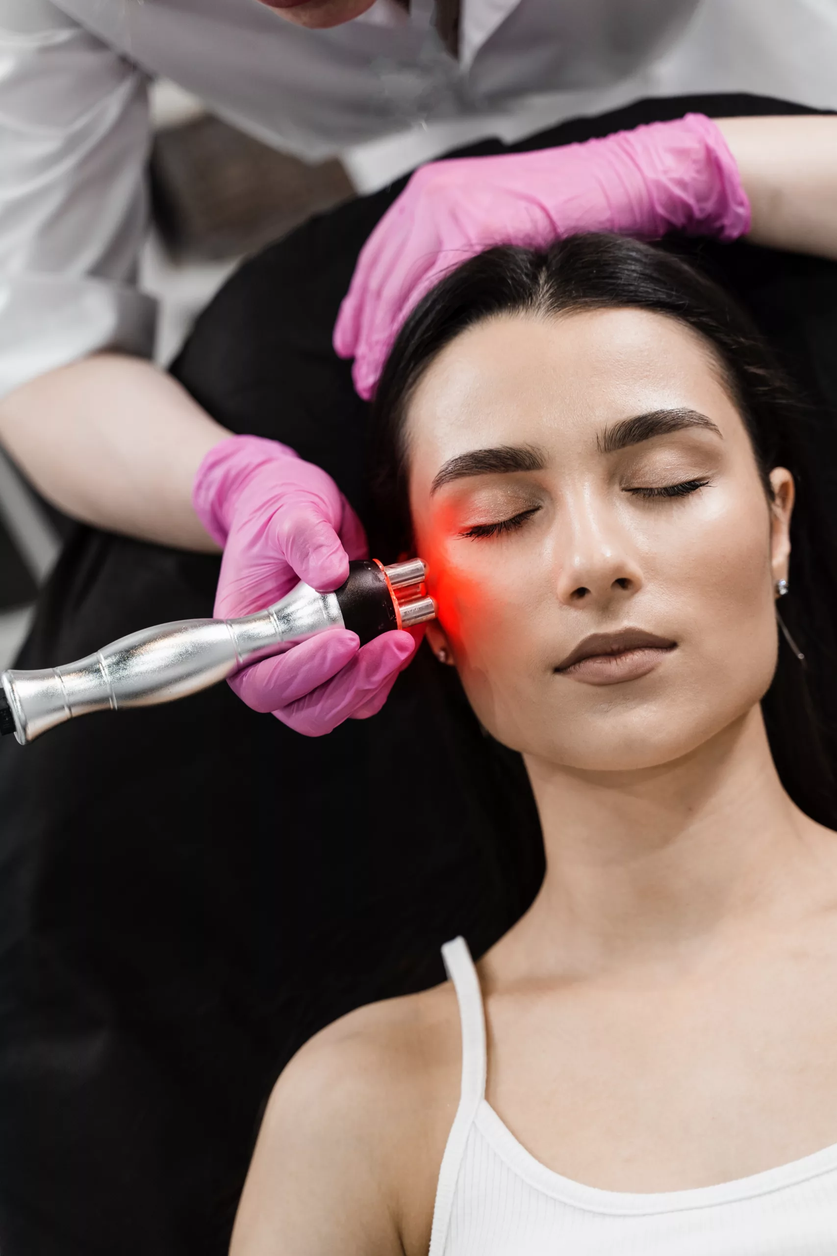 Radio frequency lifting with red light for young woman close-up. Dermatologist is doing radio frequency RF skin tightening. RF facelift firms and lifts sagging skin.