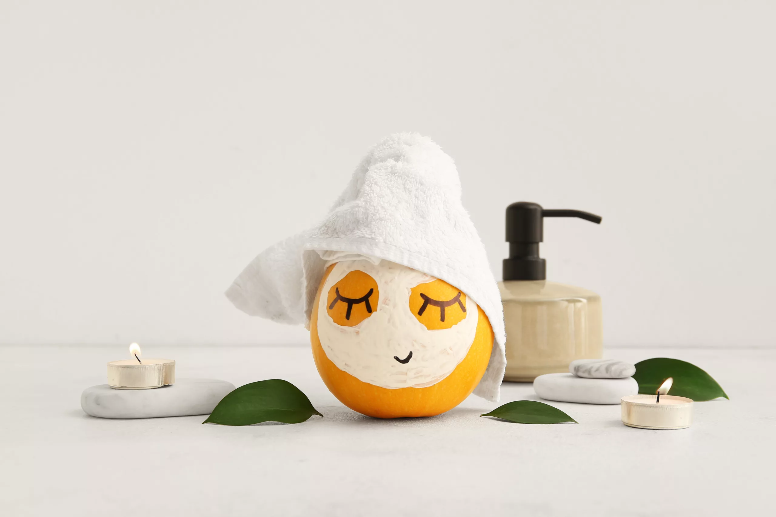 Pumpkin with mask, spa stones and leaves on light background